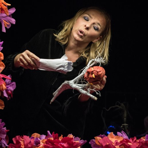Agnieszka trzyma w rękach lalkę teatralną, mówi do niej. Wokół niej kolorowe kwiaty z bibuły.