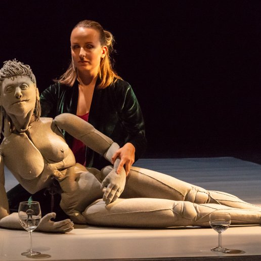 Spektakl Romans. Aktorka i lalka leżą na podłodze. Lalka podparta ramieniem. Przed nią kieliszek z wodą.