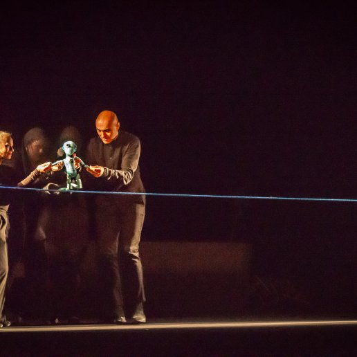 Spektakl "Blaski i cienie". Aktorzy animują niewielkich rozmiarów niebieską lalką człowieka. Lalka tańczy na linie.