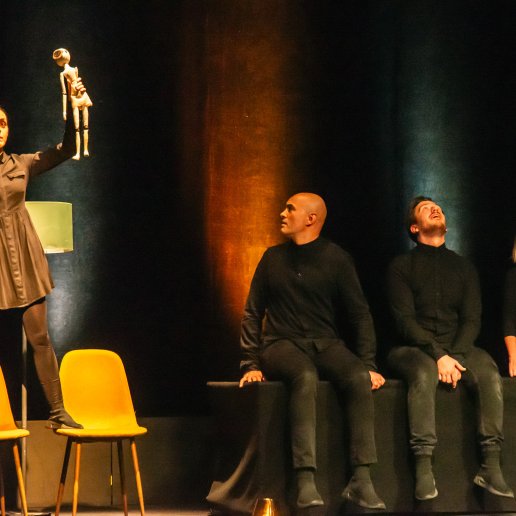 Spektakl "Blaski i cienie". Aktorka stoi na krześle, trzyma w ręce drewnianą lalkę. Obok niej troje aktorów, rozglądają się na boki