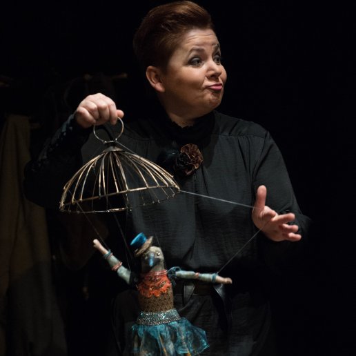 Aktorka z lalką kaczki. Trzyma lalkę za pomocą sznurków. Nad głową kaczki fragment klatki dla ptaków.
