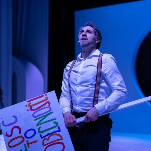 Aktor trzyma transparent z kolorowym napisem MIŁOŚC TO OBECNOŚĆ.