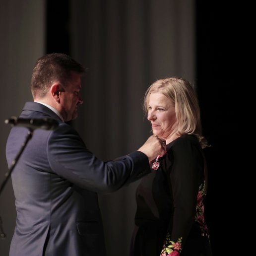 Agnieszka stoi na scenie wraz z Wicewojewodą Opolskim Piotrem Pośpiechem, który mówi wpina Agnieszce Brązowy Medal Zasłużony Kulturze Gloria Artis.