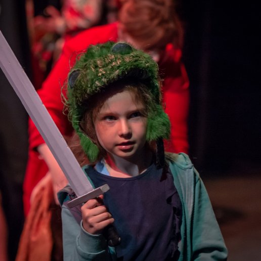 Dziewczynka ma na głowie zieloną futrzastą czapką a w dłoni trzyma miecz.
