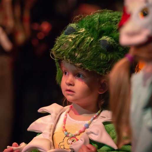 Dziewczynka z fantazyjna czapką teatralną. Czapka jest zielona i włochata.