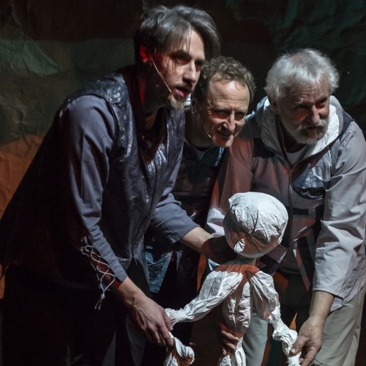 Trzech aktorów mężczyzn trzyma dużą papierową lalkę. Patrzą w tym samym kierunku.