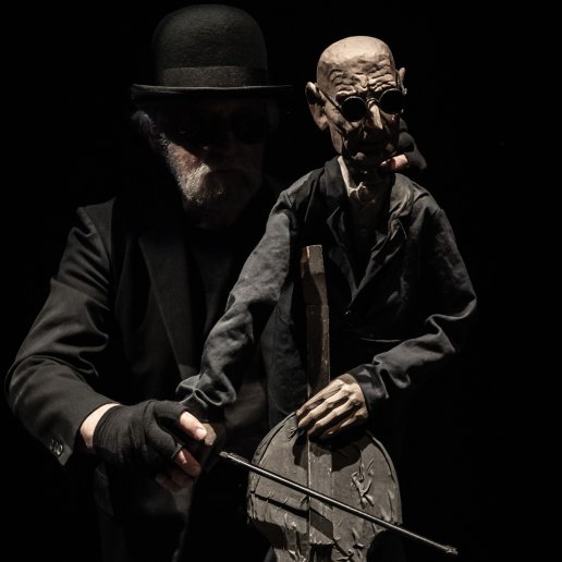 Aktor animuje lalką starszego mężczyzny, który gra na wiolonczeli, ma ciemne okulary i jest niewidomy.