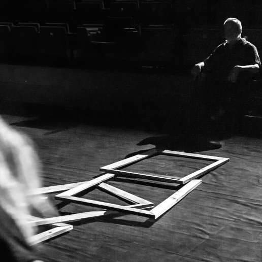 Na środku scenicznej podłogi leżą drewniane ramy obrazów. Przy nich aktorka. Reżyser siedzi na widowni.